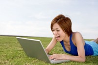 Japanese woman on grass happily looking at laptop