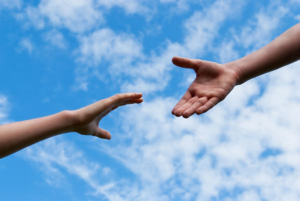 Two hands reaching out with sky in the background